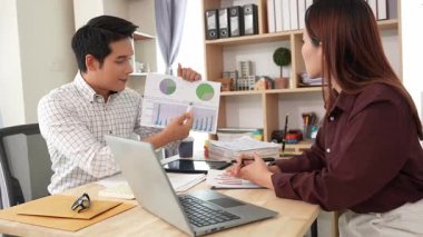 Ev konferans odasında yapılan toplantı sırasında artan satış, gelir ve kâr verilerini inceleyen ve analiz eden iki işadamı ve kadının görüntüsü.