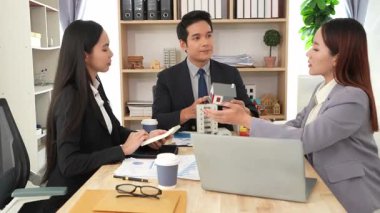 Emlakçı borç para alıyor ve bir mülk için nakit ödüyor. Emlakçı müşterilere ev planlarını sunar. Ev alırken ya da satarken karı koca.