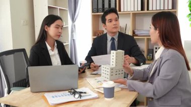 Emlakçı borç para alıyor ve bir mülk için nakit ödüyor. Emlakçı müşterilere ev planlarını sunar. Ev alırken ya da satarken karı koca.