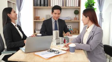 Emlakçı borç para alıyor ve bir mülk için nakit ödüyor. Emlakçı müşterilere ev planlarını sunar. Ev alırken ya da satarken karı koca.