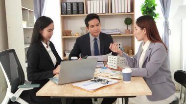 Emlakçı borç para alıyor ve bir mülk için nakit ödüyor. Emlakçı müşterilere ev planlarını sunar. Ev alırken ya da satarken karı koca.