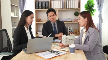 Emlakçı borç para alıyor ve bir mülk için nakit ödüyor. Emlakçı müşterilere ev planlarını sunar. Ev alırken ya da satarken karı koca.