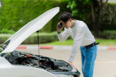 Genç bir adam sigorta acentesini aramak için telefonunu kullanıyor. Arabası bir kazada hasar görmüş..