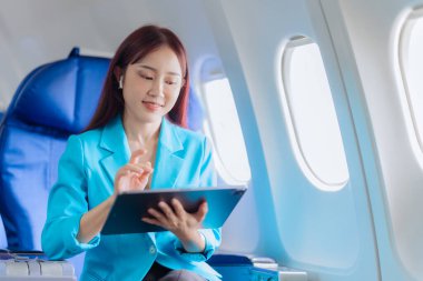 Pencere kenarındaki uçakta tek başına oturup sosyal ağlardan haberler okuyan ya da uçakta seyahat uygulamaları kullanan mutlu genç bir kadın..