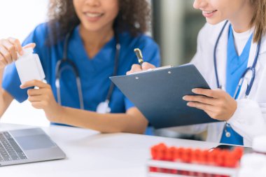 İki kadın bilim adamı modern bir laboratuvarda test tüplerindeki sıvıları inceliyor, özel koruyucu giysiler giyerken kimyasalları ve deneysel maddeleri inceliyor..