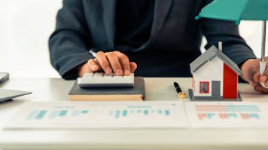 Emlakçı evin maliyetini hesaplamak için hesap makinesi kullanır. Sözleşmeli belgelerle çevrili modern evin minyatür maketi başarılı gayrimenkul satışlarını gösteriyor..