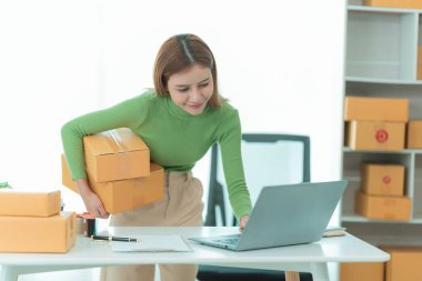 Güzel Asyalı kadın telefonda müşteri adreslerini kontrol ederken gülümsüyor. Çevrimiçi e-ticaret mağazası, ürünler satmak, nakliye.