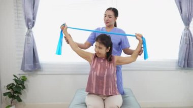 Üst düzey bir kadın, genç bir hemşireyle egzersiz yapıyor. Yaşlı bir kadına evde koltukta oturmasında yardım ediyor. Sağlık danışmanlığı, fizik tedavi konsepti.