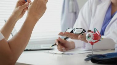 Kadın doktor danışmanlık için göz modelini tutuyor. Yaşlı bir kadın görüşü hakkında doktora danışıyor. Yaşlılar için tıbbi teşhis. Anatomi. Göz modeli.