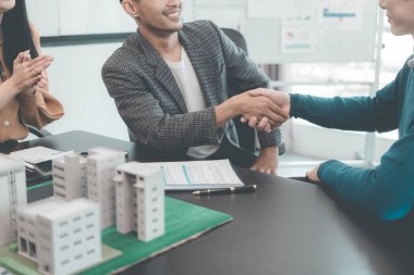 Emlak işçileri, sözleşmeli bir müşteriyle ev satma anlaşması yapmak için el sıkışıyor..