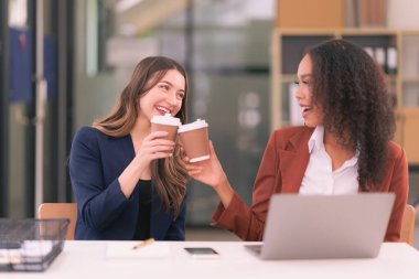 Takım elbiseli iki iş kadını bilgisayar teknolojisi belgelerini kullanarak modern ofisteki analiz için beyin fırtınası yapıyorlar.