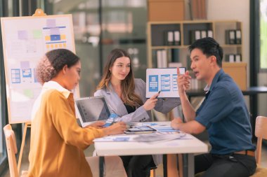 Bir grup iş adamı, ofiste tabletle çalışan grafik tasarımlı başarılı takım çalışmasının sonucunu temsil eden bir ürün tasarlıyor..