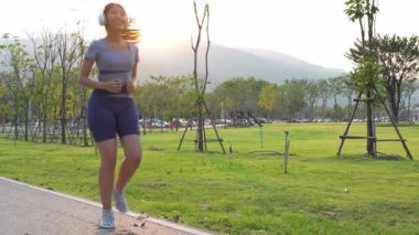 Güzel Asyalı bayan koşucu yazın parkta koşuyor, pozitif bir tavırla sağlıklı bir hayat sürüyor. Egzersiz rahatlatıcı ve mutludur..