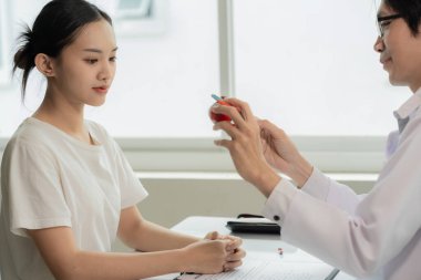 Glukoma, Katarakt, Retina Erkek Göz Hastalıkları Uzmanı, bir hastane muayene odasındaki muayene masasındaki Asyalı bir kadın hastaya göz modeli kullanarak göz hastalığını açıklıyor..