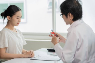 Glukoma, Katarakt, Retina Erkek Göz Hastalıkları Uzmanı, bir hastane muayene odasındaki muayene masasındaki Asyalı bir kadın hastaya göz modeli kullanarak göz hastalığını açıklıyor..