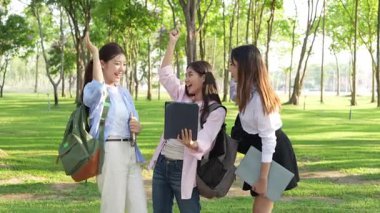 Bir grup Asyalı kız öğrenci akademik içeriği araştırmayı tartışıyor, tabletleri kullanıyor, parktaki bir ağacın altındaki not defterlerine not alıyorlar..