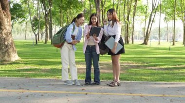 Bir grup Asyalı kız öğrenci akademik içeriği araştırmayı tartışıyor, tabletleri kullanıyor, parktaki bir ağacın altındaki not defterlerine not alıyorlar..