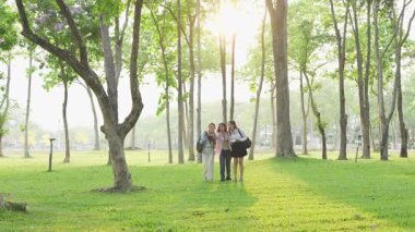 Bir grup Asyalı kız öğrenci akademik içeriği araştırmayı tartışıyor, tabletleri kullanıyor, parktaki bir ağacın altındaki not defterlerine not alıyorlar..
