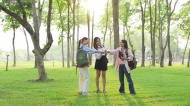 Bir grup Asyalı kız öğrenci akademik içeriği araştırmayı tartışıyor, tabletleri kullanıyor, parktaki bir ağacın altındaki not defterlerine not alıyorlar..