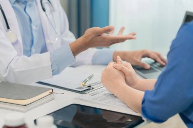 Muayene sırasında klinikte masasında oturan dost canlısı erkek doktorun tavsiyelerini dinleyen genç bayan hasta görüntüsü. Kapat..