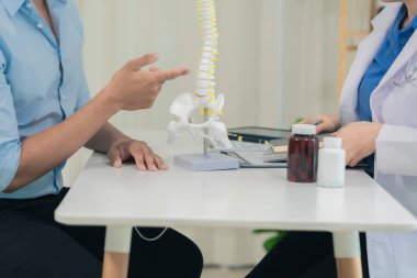 Hasta ve ortopedist, doktorun ofisinde insan iskeleti modelini tartışıyor ve hastanın tedavisini tartışıyor..