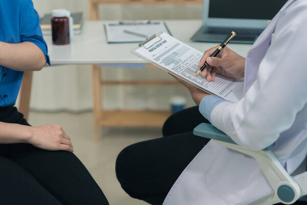 Изображение молодой пациентки в офисе, слушающей советы дружелюбного врача-мужчины, сидящего за столом в клинике во время физического осмотра. Закрыть.