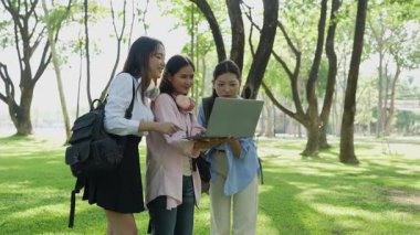 Laptopları ve tablet bilgisayarları olan bir grup üniversite öğrencisi parkta ödev yapıyor, dışarıda bir ağacın altında konuşuyor ve birlikte çalışıyorlar..