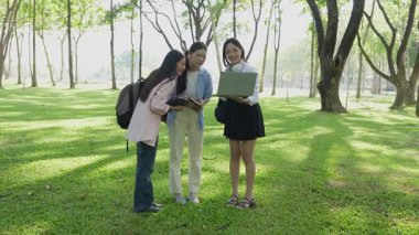 Laptopları ve tablet bilgisayarları olan bir grup üniversite öğrencisi parkta ödev yapıyor, dışarıda bir ağacın altında konuşuyor ve birlikte çalışıyorlar..