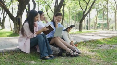 Laptopları ve tablet bilgisayarları olan bir grup üniversite öğrencisi parkta ödev yapıyor, dışarıda bir ağacın altında konuşuyor ve birlikte çalışıyorlar..