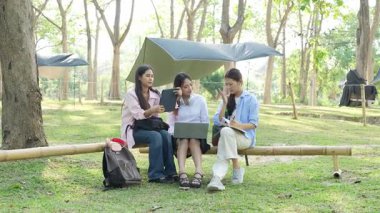 Laptopları ve tablet bilgisayarları olan bir grup üniversite öğrencisi parkta ödev yapıyor, dışarıda bir ağacın altında konuşuyor ve birlikte çalışıyorlar..
