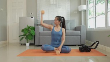 Elinde dambıl tutan Asyalı kadın sağlık için egzersiz yapıyor. Spor kıyafetlerinde, oturma odasında halterlerle egzersiz yaparken. Sağlık konsepti, kilo kaybı.