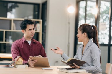 Emlakçılar müşterilerine bir konferans odasında ev planları gösteriyorlar. Alıcılar iş sözleşmelerini ev ofisinde imzalarlar ve kira, konut kredisi veya ev sigortası almaktan tasarruf etmeyi tartışırlar.