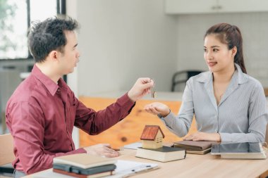 Emlakçılar müşterilerine bir konferans odasında ev planları gösteriyorlar. Alıcılar iş sözleşmelerini ev ofisinde imzalarlar ve kira, konut kredisi veya ev sigortası almaktan tasarruf etmeyi tartışırlar.