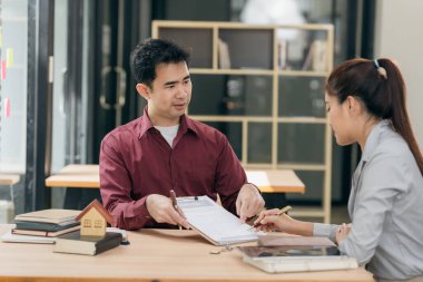 Emlakçılar müşterilerine bir konferans odasında ev planları gösteriyorlar. Alıcılar iş sözleşmelerini ev ofisinde imzalarlar ve kira, konut kredisi veya ev sigortası almaktan tasarruf etmeyi tartışırlar.