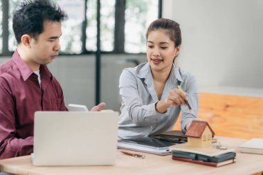 Emlakçılar müşterilerine bir konferans odasında ev planları gösteriyorlar. Alıcılar iş sözleşmelerini ev ofisinde imzalarlar ve kira, konut kredisi veya ev sigortası almaktan tasarruf etmeyi tartışırlar.