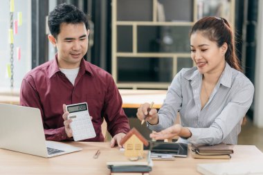 Emlakçılar müşterilerine bir konferans odasında ev planları gösteriyorlar. Alıcılar iş sözleşmelerini ev ofisinde imzalarlar ve kira, konut kredisi veya ev sigortası almaktan tasarruf etmeyi tartışırlar.