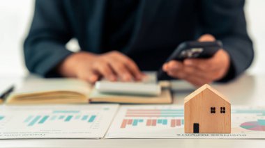 Emlakçı, masa başında minyatür ev modeli kullanan, emlak yatırımını temsil eden, ev satın alan, dükkanı kapatan bir bilgisayar kullanıyor..