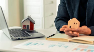 Emlakçı, masa başında minyatür ev modeli kullanan, emlak yatırımını temsil eden, ev satın alan, dükkanı kapatan bir bilgisayar kullanıyor..