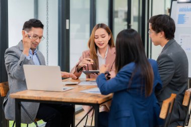 Bir grup Asyalı iş adamı başarılı iş yatırımlarının sonuçlarını ve başarılı takım çalışmalarının sonuçlarını gösteren grafikler ve grafikleri tartışıyor.