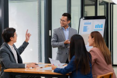 Bir grup Asyalı iş adamı başarılı iş yatırımlarının sonuçlarını ve başarılı takım çalışmalarının sonuçlarını gösteren grafikler ve grafikleri tartışıyor.