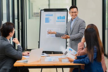 Bir grup Asyalı iş adamı başarılı iş yatırımlarının sonuçlarını ve başarılı takım çalışmalarının sonuçlarını gösteren grafikler ve grafikleri tartışıyor.