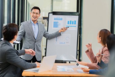 Bir grup Asyalı iş adamı başarılı iş yatırımlarının sonuçlarını ve başarılı takım çalışmalarının sonuçlarını gösteren grafikler ve grafikleri tartışıyor.