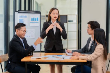 Bir grup Asyalı iş adamı başarılı iş yatırımlarının sonuçlarını ve başarılı takım çalışmalarının sonuçlarını gösteren grafikler ve grafikleri tartışıyor.