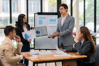 Bir grup Asyalı iş adamı başarılı iş yatırımlarının sonuçlarını ve başarılı takım çalışmalarının sonuçlarını gösteren grafikler ve grafikleri tartışıyor.