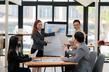 Bir grup Asyalı iş adamı başarılı iş yatırımlarının sonuçlarını ve başarılı takım çalışmalarının sonuçlarını gösteren grafikler ve grafikleri tartışıyor.