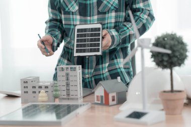İki mühendis rüzgar türbini model bileşenleri üzerinde çalışıyor ve çözümün yenilenebilir enerji kaynaklarını bilgisayarla tartışıyor. Sürdürülebilir enerji projeleri geliştirmek için rüzgar türbini güneş paneli modeli.