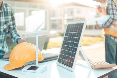 İki mühendis rüzgar türbini model bileşenleri üzerinde çalışıyor ve çözümün yenilenebilir enerji kaynaklarını bilgisayarla tartışıyor. Sürdürülebilir enerji projeleri geliştirmek için rüzgar türbini güneş paneli modeli.