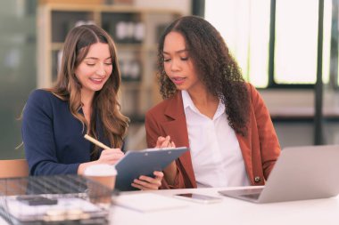 İki Asyalı iş kadını, dokümanlar ve grafiklerle işbirliği yapmak ve onları analiz etmek ve yeni iş projeleri stratejilerini tartışmak için dizüstü bilgisayar ve tablet kullanıyorlar..