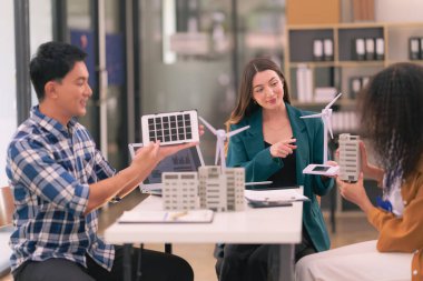 Rüzgâr ve güneş enerjisi kullanarak yenilenebilir enerji tasarlamak için güneş panelleri olan masaların üzerine ev modelleri ve planlarla rüzgar türbinleriyle buluşan mühendisler..