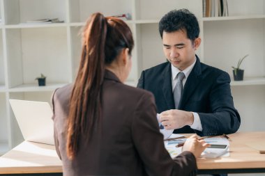 İki Asyalı işadamı başarılı takım çalışmalarının sonuçlarını gösteren çizelge ve grafikleri tartışıyor. İşyerinde çizelge tabletleri ve tabletler kullanılıyor